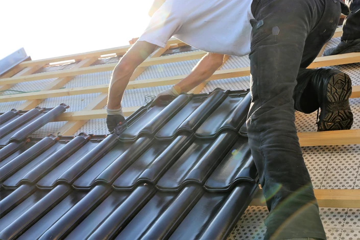 Chantier de couverture en extérieur avec deux couvreurs installant des tuiles métalliques grises sur charpente bois