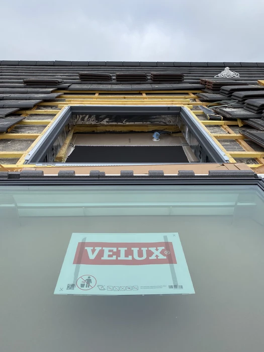 Vue en contre-plongée d'une installation de fenêtre de toit VELUX en cours de pose sur une toiture en ardoises noires