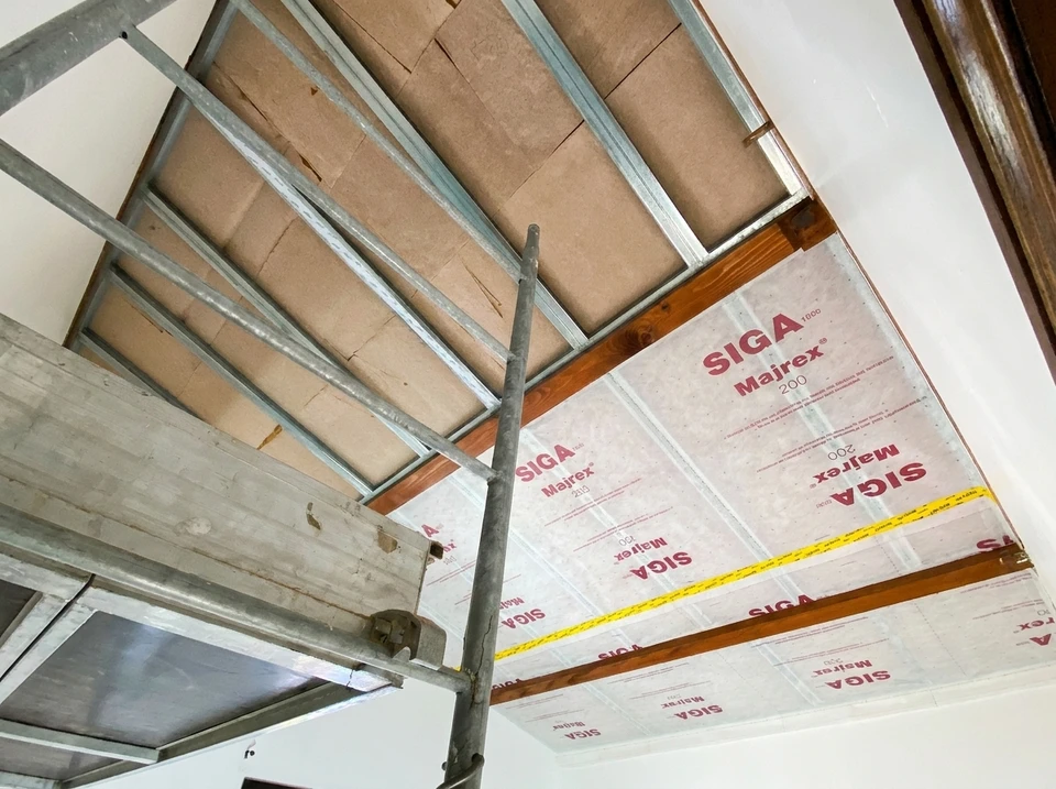 Intérieur de bâtiment en construction avec ouvrier appliquant de l'isolant thermique vert sur les murs entre les montants en bois